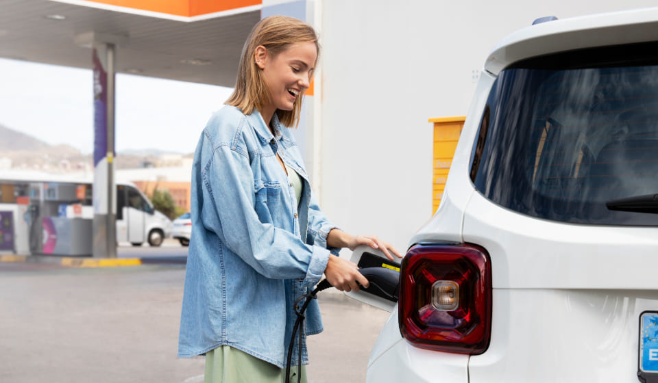 ¿Cuánto cuesta cargar un coche eléctrico en una gasolinera? Mujer cargado coche eléctrico en una gasolinera